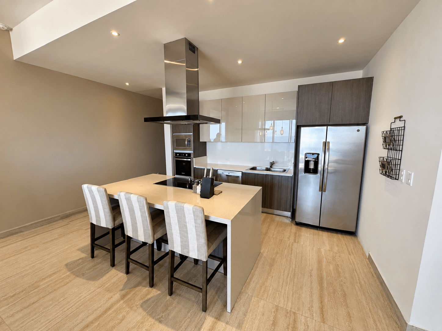 Kitchen with bar-style island, three stools, and stainless steel fridge.