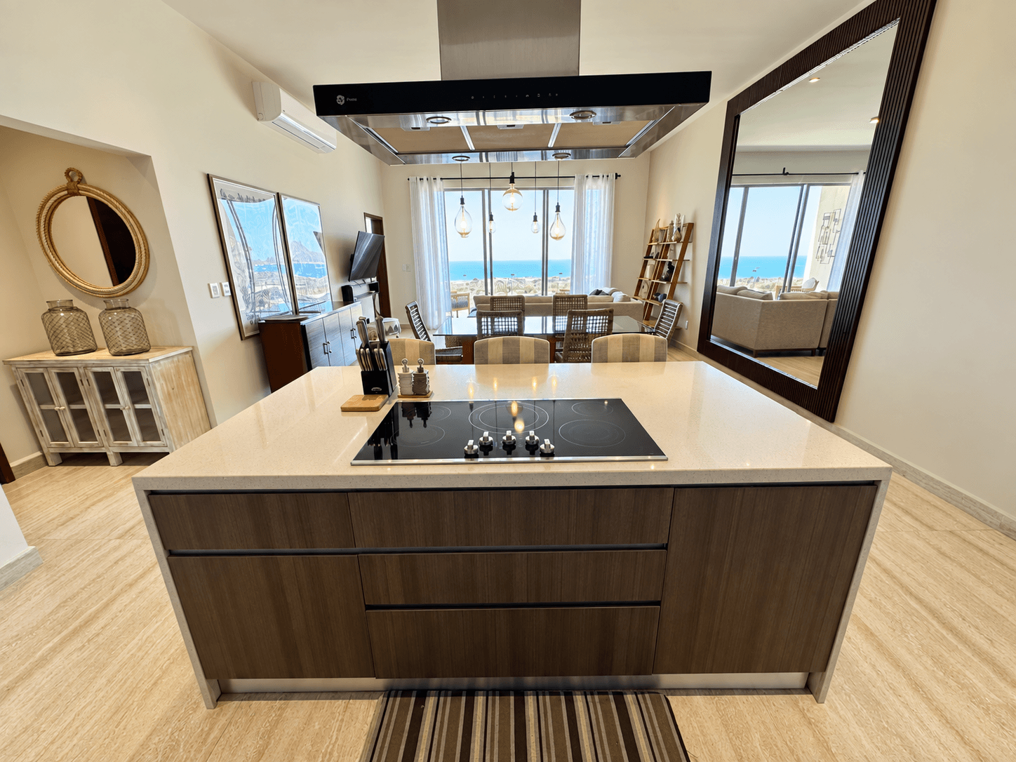 Kitchen with island and steel range hood, open view to the dining area and ocean.